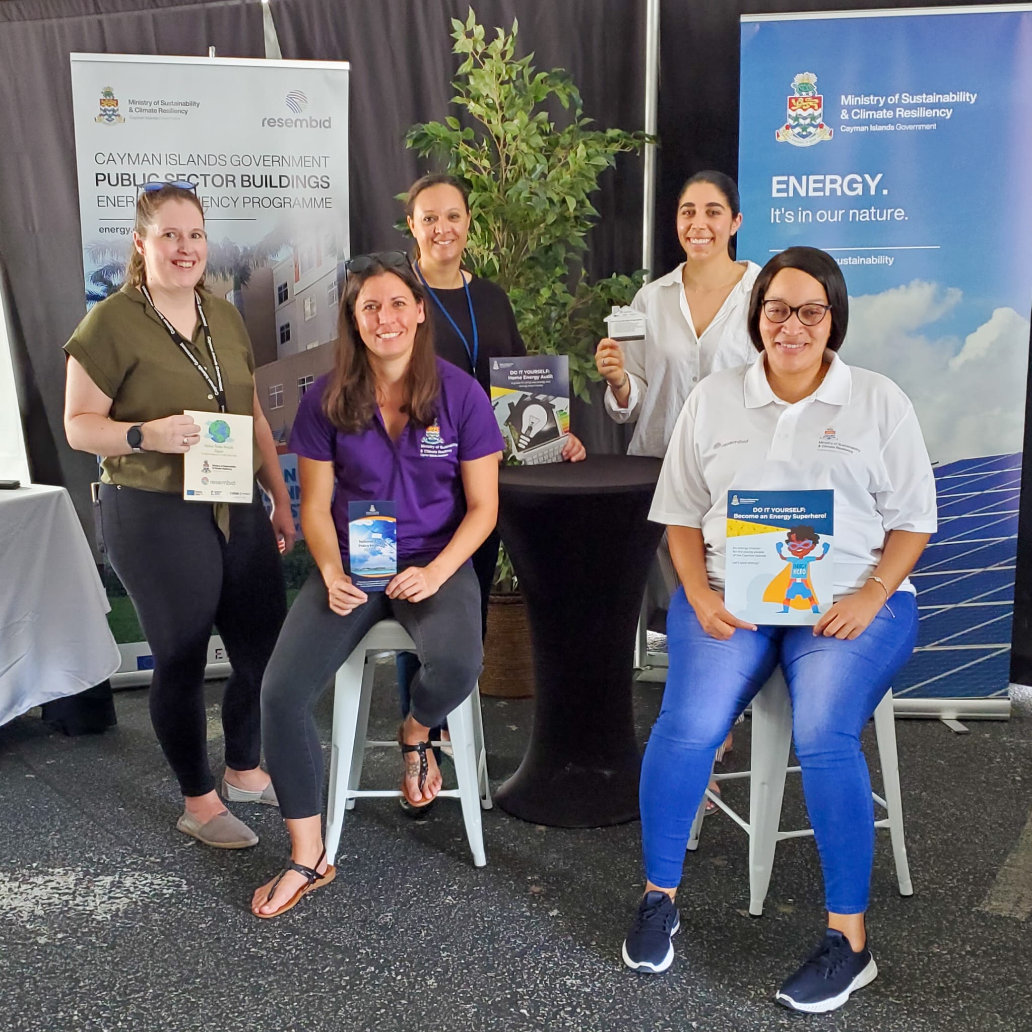 Civil Servants from the Ministry of Sustainability Climate Resiliency and Wellness pose for a picture displaying info cards, brouchures and other resources at the 2024 Builders Expo held in Grand Cayman in collaboration with RESEMBID to make housing in the Cayman Islands more energy effiecient and affordable to residents.