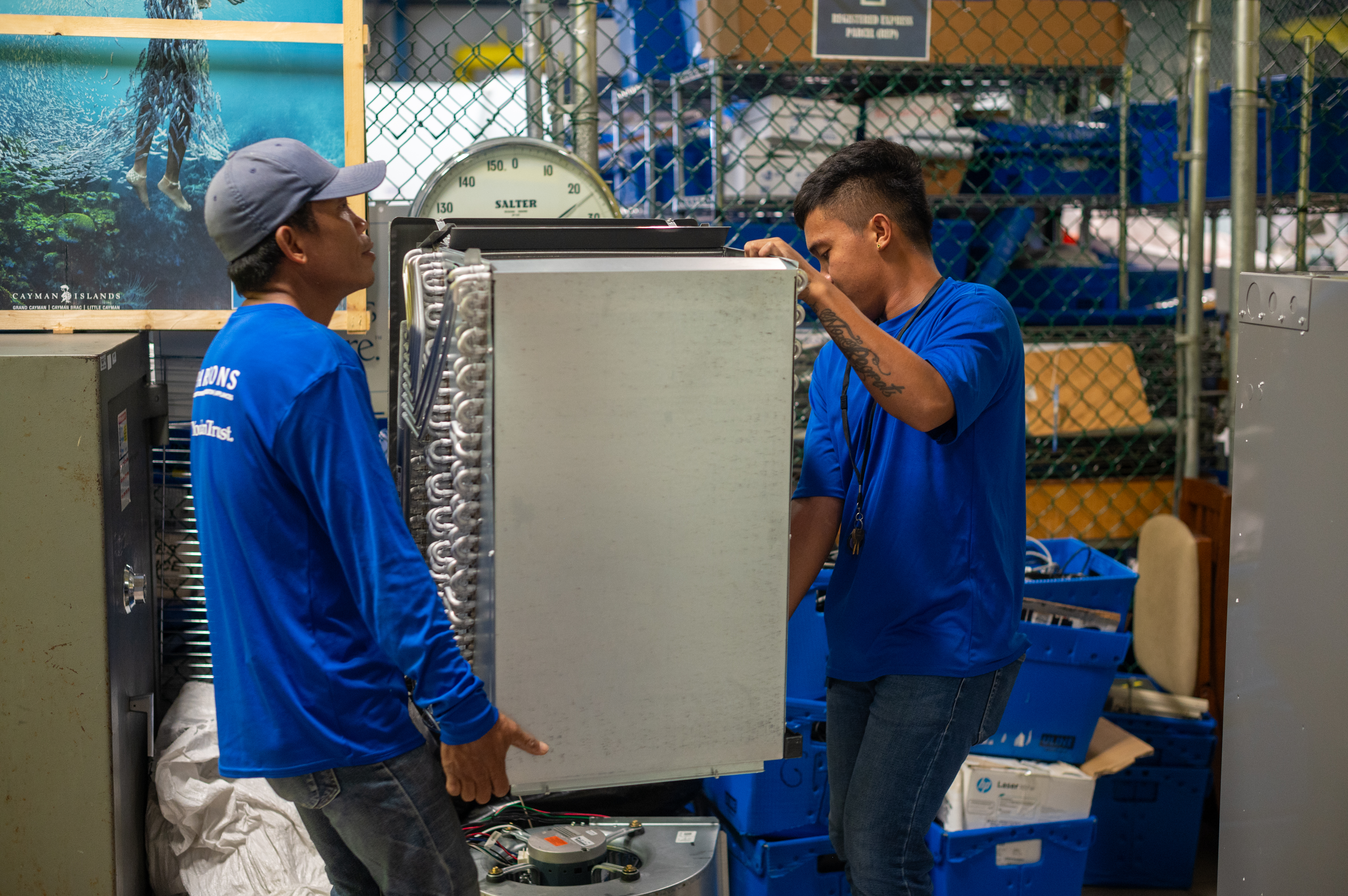Workers moving an air condintioning (AC) unit preparing for installation as part of improving energy effiency in the cayman islands.