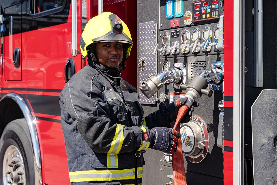 Cayman Islands Fire Service Firefighter connecting hose to fire truck.